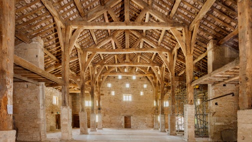 Interior of a large historic barn with exposed timber beams, stone walls, and high vaulted roof.